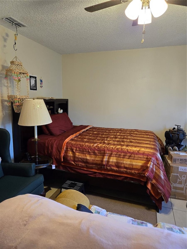 tiled bedroom with a ceiling fan, visible vents, and a textured ceiling