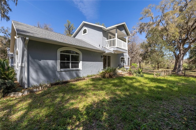 view of side of property featuring a yard, roof with shingles, a balcony, and stucco siding