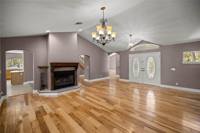 unfurnished living room featuring a high end fireplace, arched walkways, vaulted ceiling, and light wood finished floors