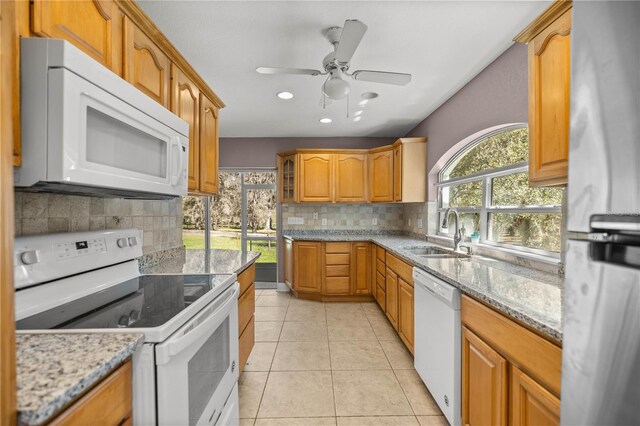 kitchen featuring light tile patterned floors, white appliances, a sink, and light stone countertops