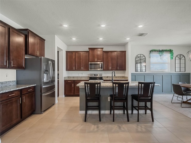 kitchen with a sink, visible vents, appliances with stainless steel finishes, light stone countertops, and a kitchen bar