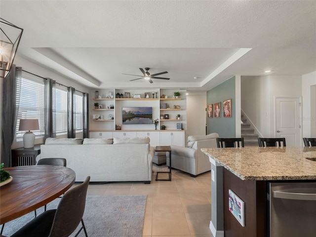 living area with light tile patterned floors, ceiling fan, stairway, a tray ceiling, and a textured ceiling