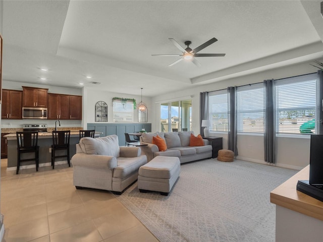 living area with ceiling fan, light tile patterned flooring, recessed lighting, baseboards, and a raised ceiling