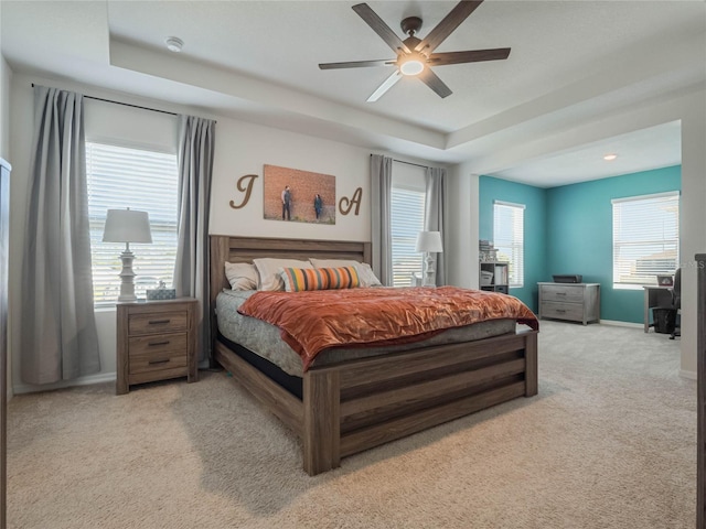 carpeted bedroom featuring a tray ceiling, a ceiling fan, and baseboards