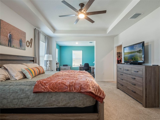 bedroom with light carpet, a tray ceiling, visible vents, and baseboards