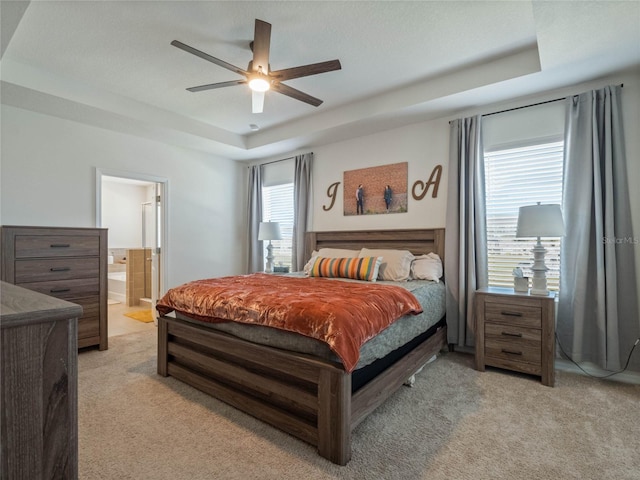 bedroom featuring a raised ceiling, light carpet, ceiling fan, and ensuite bathroom