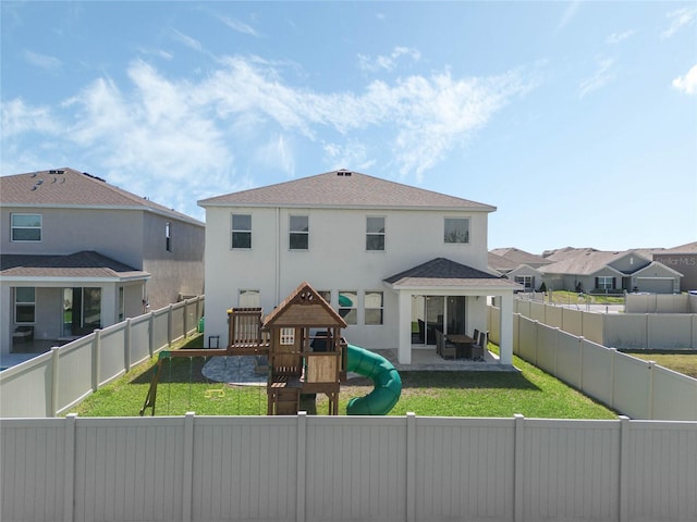 back of house featuring a lawn, a playground, a fenced backyard, and stucco siding