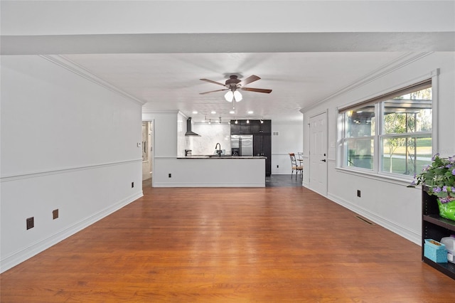 unfurnished living room with crown molding, visible vents, a ceiling fan, a sink, and wood finished floors