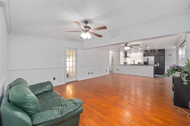 living area with a ceiling fan, crown molding, baseboards, and wood finished floors