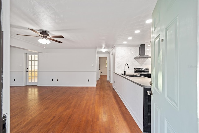 kitchen with electric range, decorative backsplash, wood finished floors, wall chimney range hood, and a sink