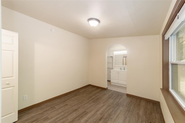 unfurnished room featuring arched walkways, baseboards, and wood finished floors