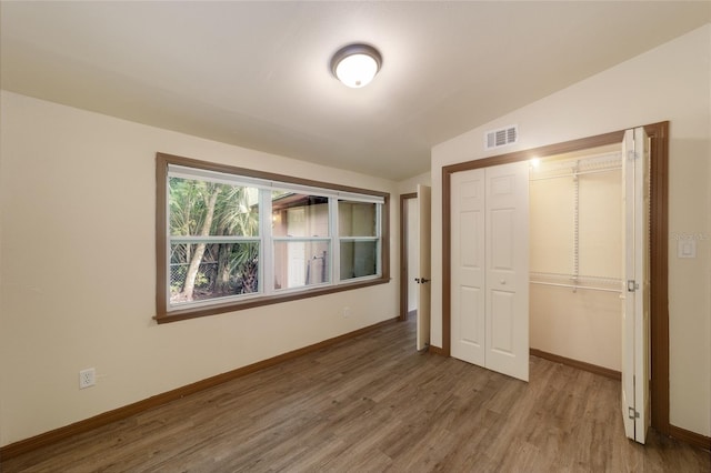 unfurnished bedroom featuring wood finished floors, visible vents, baseboards, vaulted ceiling, and a closet