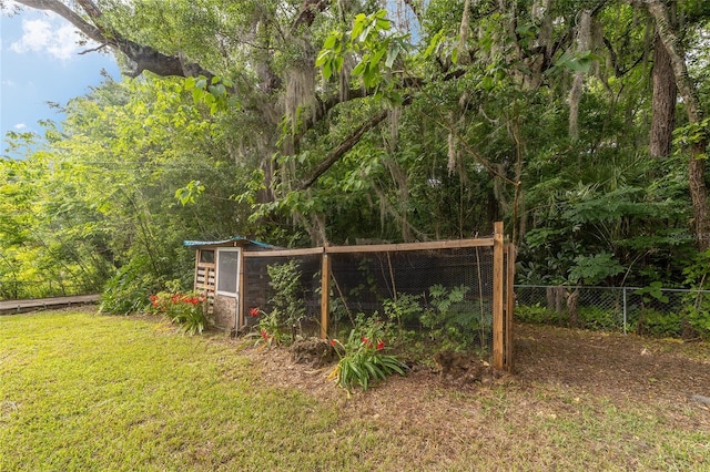 view of yard featuring a forest view, fence, a storage unit, and an outdoor structure