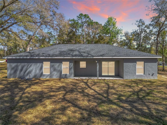 rear view of house featuring a yard, roof with shingles, a patio area, and stucco siding