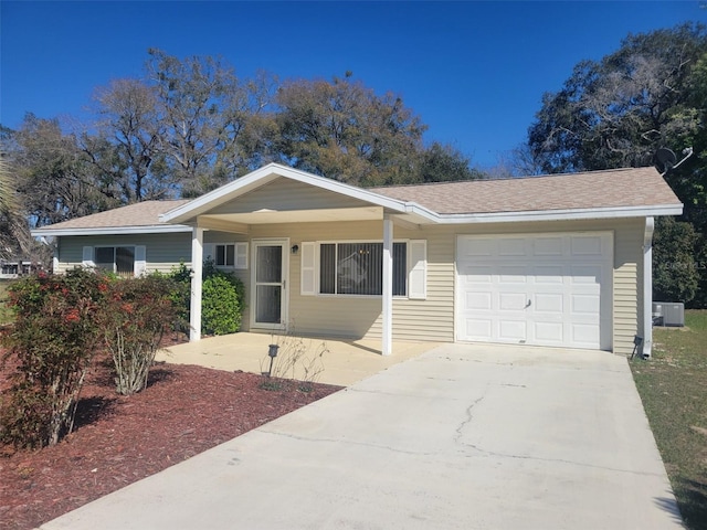 ranch-style house with a garage, a shingled roof, cooling unit, and concrete driveway