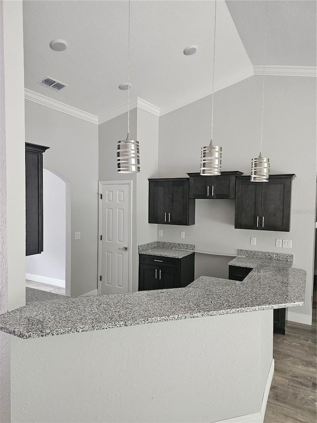 kitchen with visible vents, ornamental molding, wood finished floors, light stone countertops, and vaulted ceiling