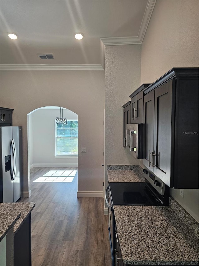 kitchen with arched walkways, crown molding, appliances with stainless steel finishes, dark wood-type flooring, and dark stone countertops