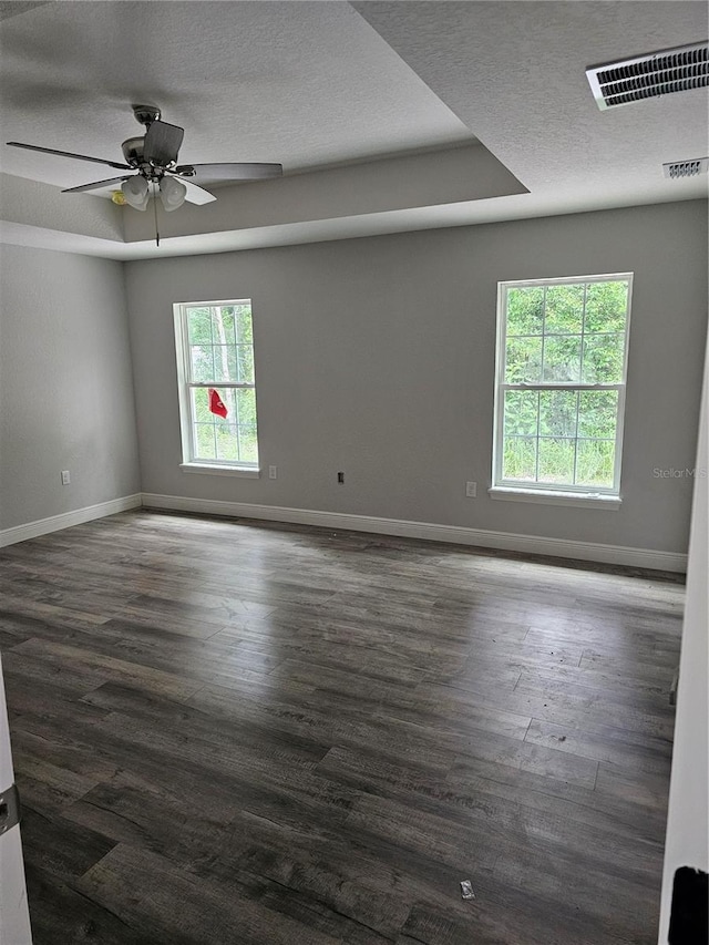 unfurnished room featuring a tray ceiling, visible vents, dark wood-type flooring, a textured ceiling, and baseboards