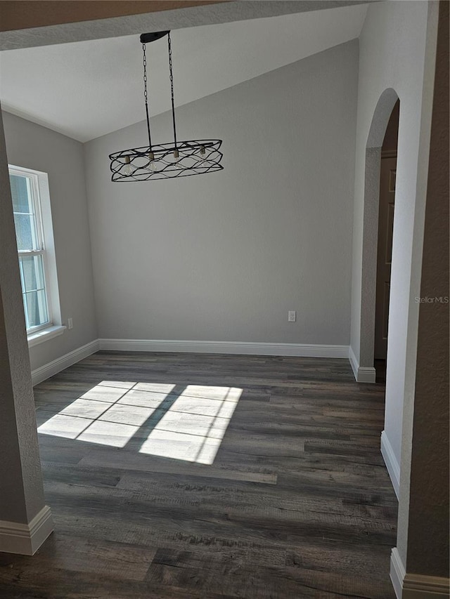 unfurnished dining area with baseboards, arched walkways, vaulted ceiling, and dark wood-style flooring