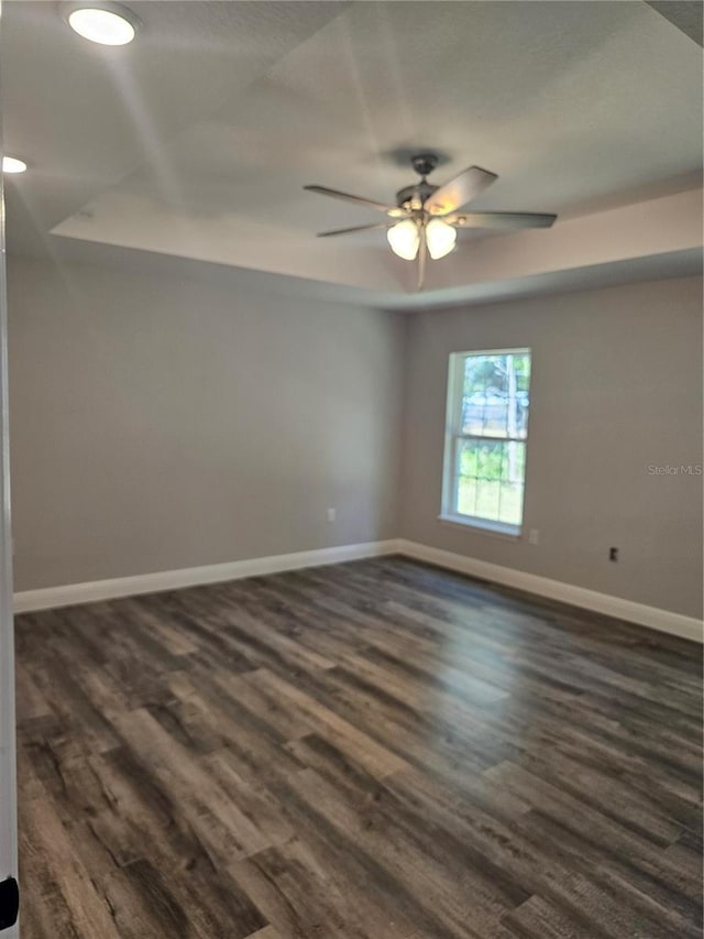 unfurnished room featuring dark wood-style floors, ceiling fan, and baseboards