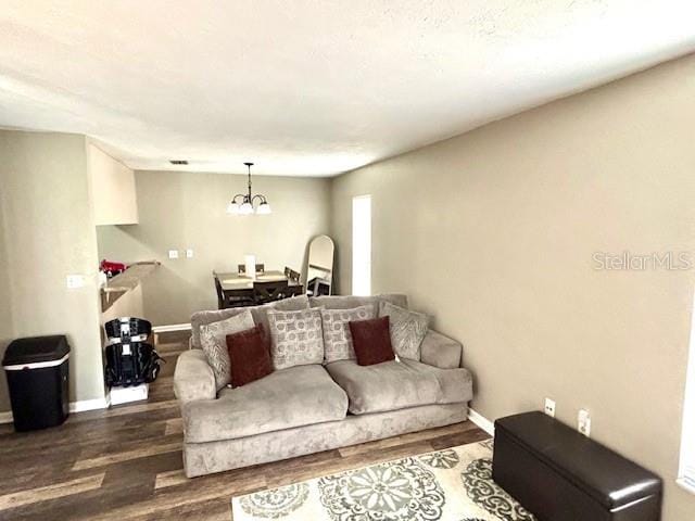 living room featuring baseboards, dark wood-style flooring, and an inviting chandelier