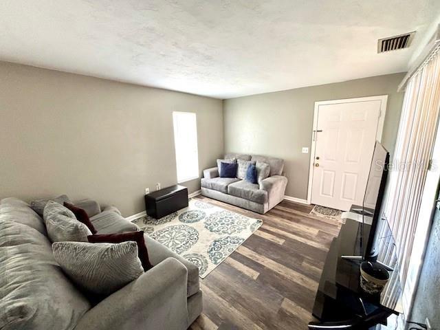 living room with baseboards, visible vents, and dark wood-style flooring