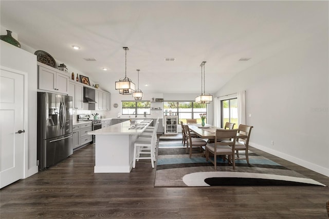 kitchen featuring appliances with stainless steel finishes, a center island, light countertops, wall chimney range hood, and a kitchen bar