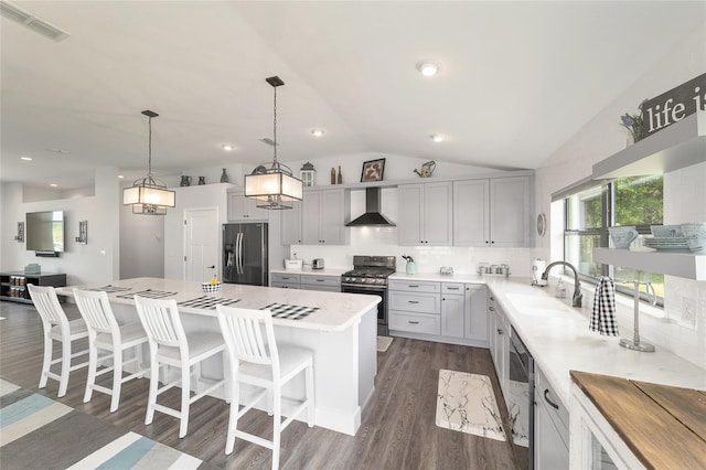 kitchen featuring a kitchen island, vaulted ceiling, stainless steel appliances, wall chimney range hood, and a sink