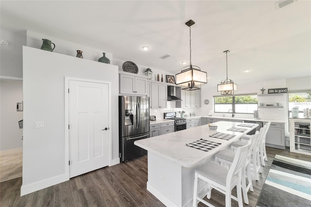 kitchen featuring gray cabinetry, open shelves, a kitchen island, appliances with stainless steel finishes, and wall chimney exhaust hood