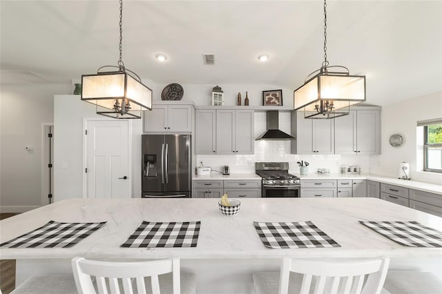 kitchen featuring gray cabinetry, appliances with stainless steel finishes, wall chimney range hood, decorative backsplash, and an inviting chandelier