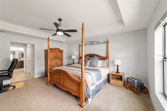 bedroom with light carpet, visible vents, baseboards, a raised ceiling, and ensuite bath