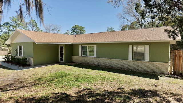 view of front of house with brick siding, roof with shingles, fence, a front yard, and stucco siding