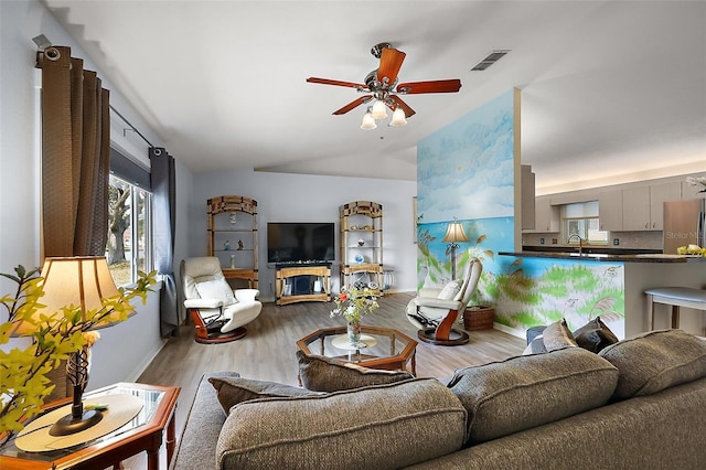 living room featuring ceiling fan, visible vents, vaulted ceiling, and wood finished floors