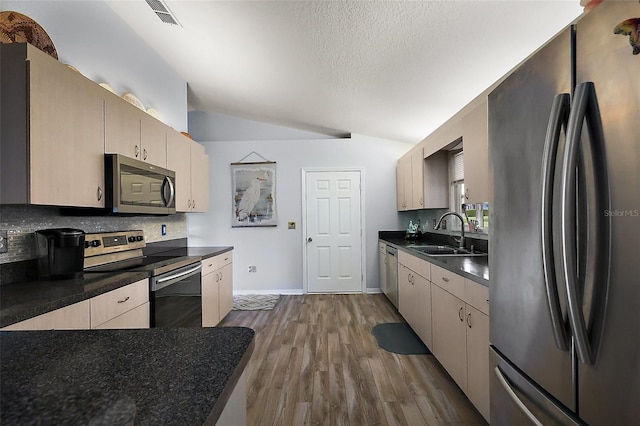 kitchen featuring dark countertops, visible vents, appliances with stainless steel finishes, vaulted ceiling, and a sink