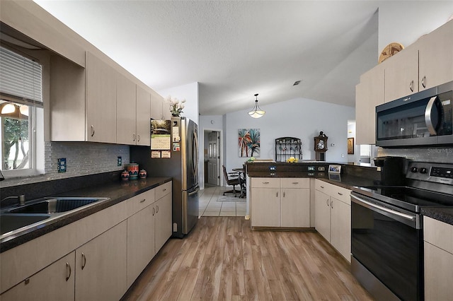 kitchen with dark countertops, lofted ceiling, light wood-style flooring, a peninsula, and stainless steel appliances