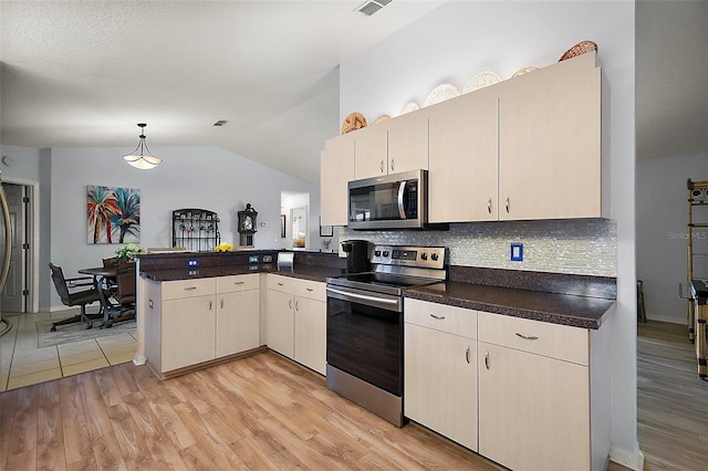 kitchen with appliances with stainless steel finishes, vaulted ceiling, light wood-style floors, and a peninsula