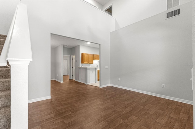 unfurnished living room with visible vents, stairway, a high ceiling, dark wood-type flooring, and baseboards