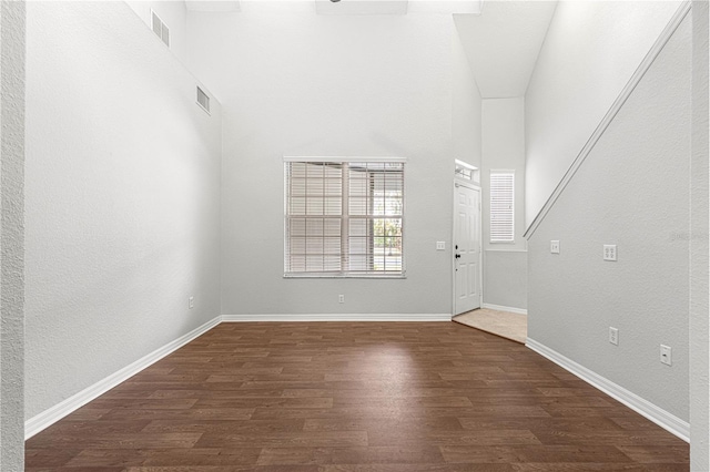 interior space featuring dark wood-style floors, visible vents, a towering ceiling, and baseboards