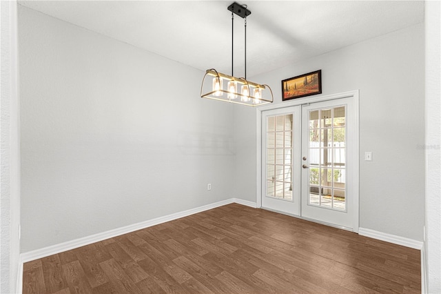 spare room featuring dark wood-type flooring, french doors, baseboards, and an inviting chandelier