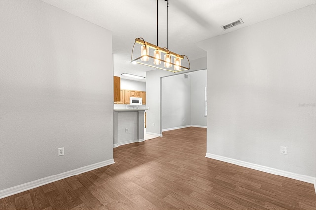 unfurnished dining area with dark wood-style flooring, visible vents, baseboards, and an inviting chandelier