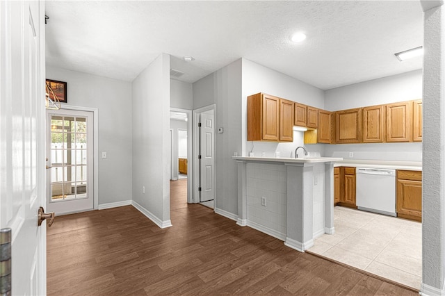 kitchen with light countertops, white dishwasher, a sink, light wood-type flooring, and a peninsula