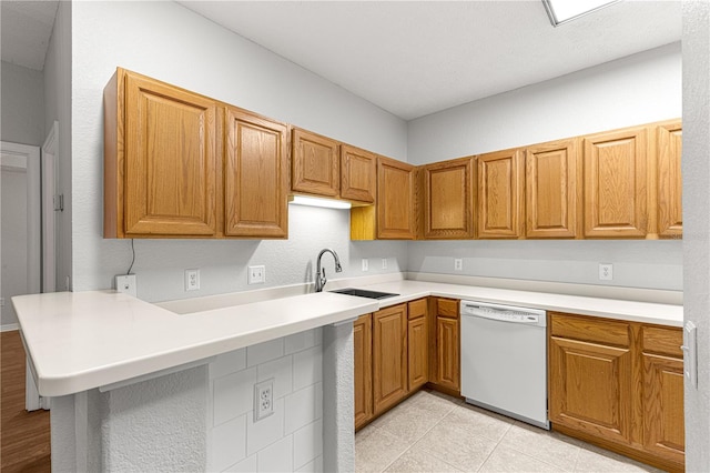 kitchen featuring brown cabinets, light countertops, a sink, dishwasher, and a peninsula