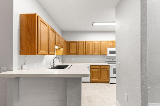 kitchen with a peninsula, white appliances, a sink, light countertops, and brown cabinets