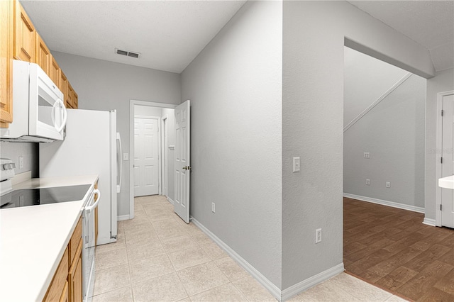 kitchen with light countertops, visible vents, light wood-style floors, white appliances, and baseboards