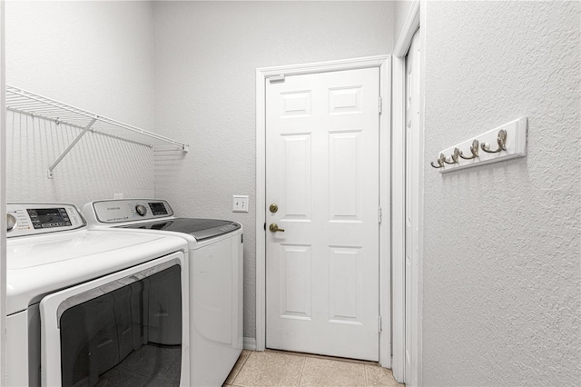 laundry room with laundry area, light tile patterned floors, a textured wall, and independent washer and dryer