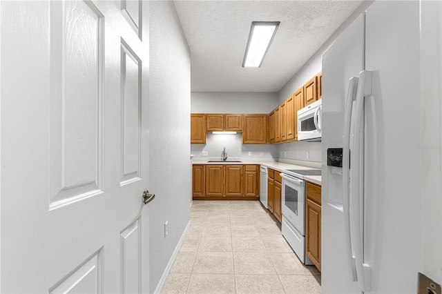 kitchen with brown cabinets, light countertops, a sink, a textured ceiling, and white appliances