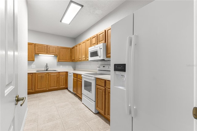 kitchen with brown cabinets, white appliances, light countertops, and a sink