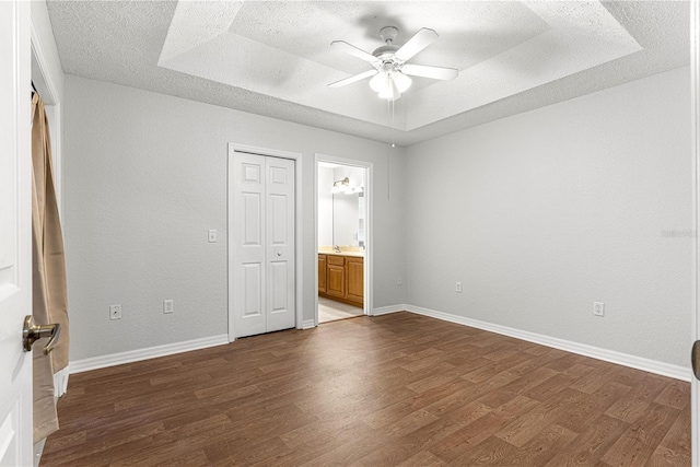 unfurnished bedroom with a raised ceiling, baseboards, a textured ceiling, and dark wood-style flooring