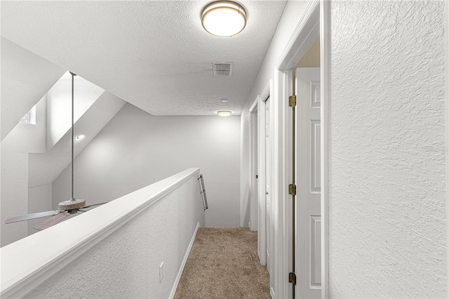 hallway featuring carpet, visible vents, a textured ceiling, and a textured wall