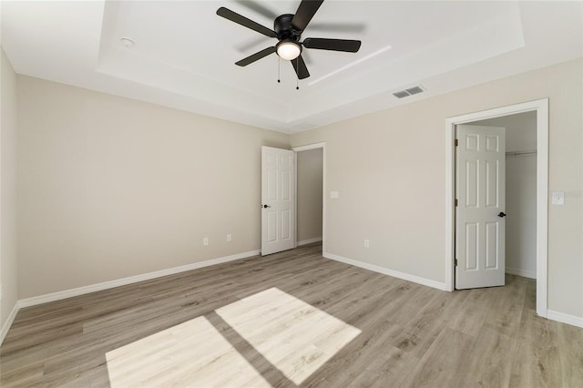 114 Bay Dr, Ocklawaha, FL 32179 - unfurnished bedroom with a tray ceiling, light wood-style floors, baseboards, and a walk in closet